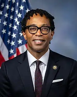 Official House portrait of Bell smiling in front of the U.S. flag, wearing a black suit, white shirt, and light green plaid tie.
