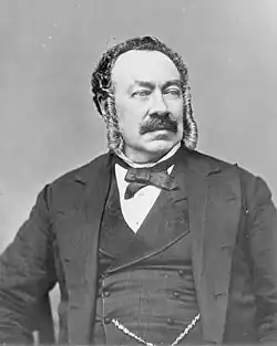 Black and white portrait photograph of a seated man with a mustache wearing a suit.