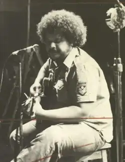 Maia, with an Afro hairstyle, playing a guitar